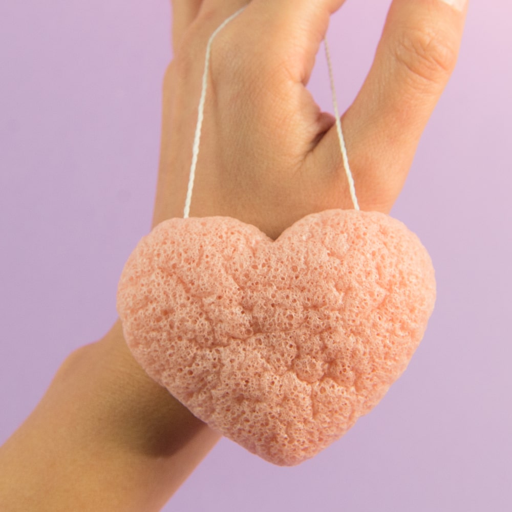 BodyBlendz pink konjac heart sponge held in hand, gentle facial exfoliator for cleansing, removing impurities, and achieving soft, smooth skin