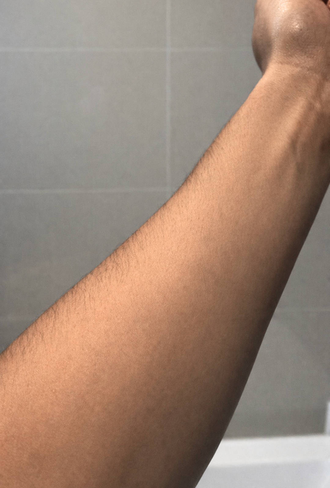 Partial view of a person's arm against a tiled wall background. An after image using the tan lotion.