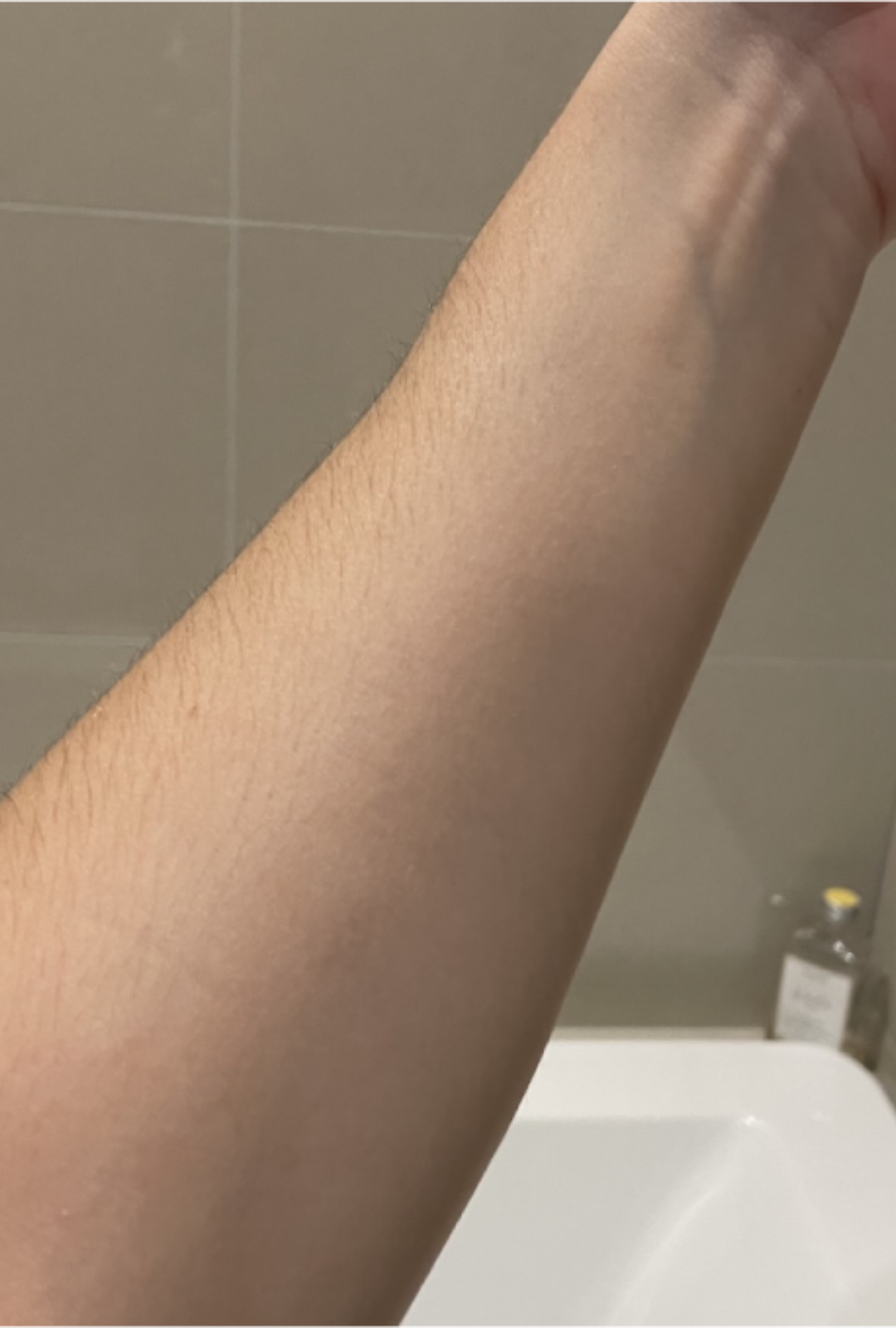 Close-up of a person's arm with visible hair against a bathroom background