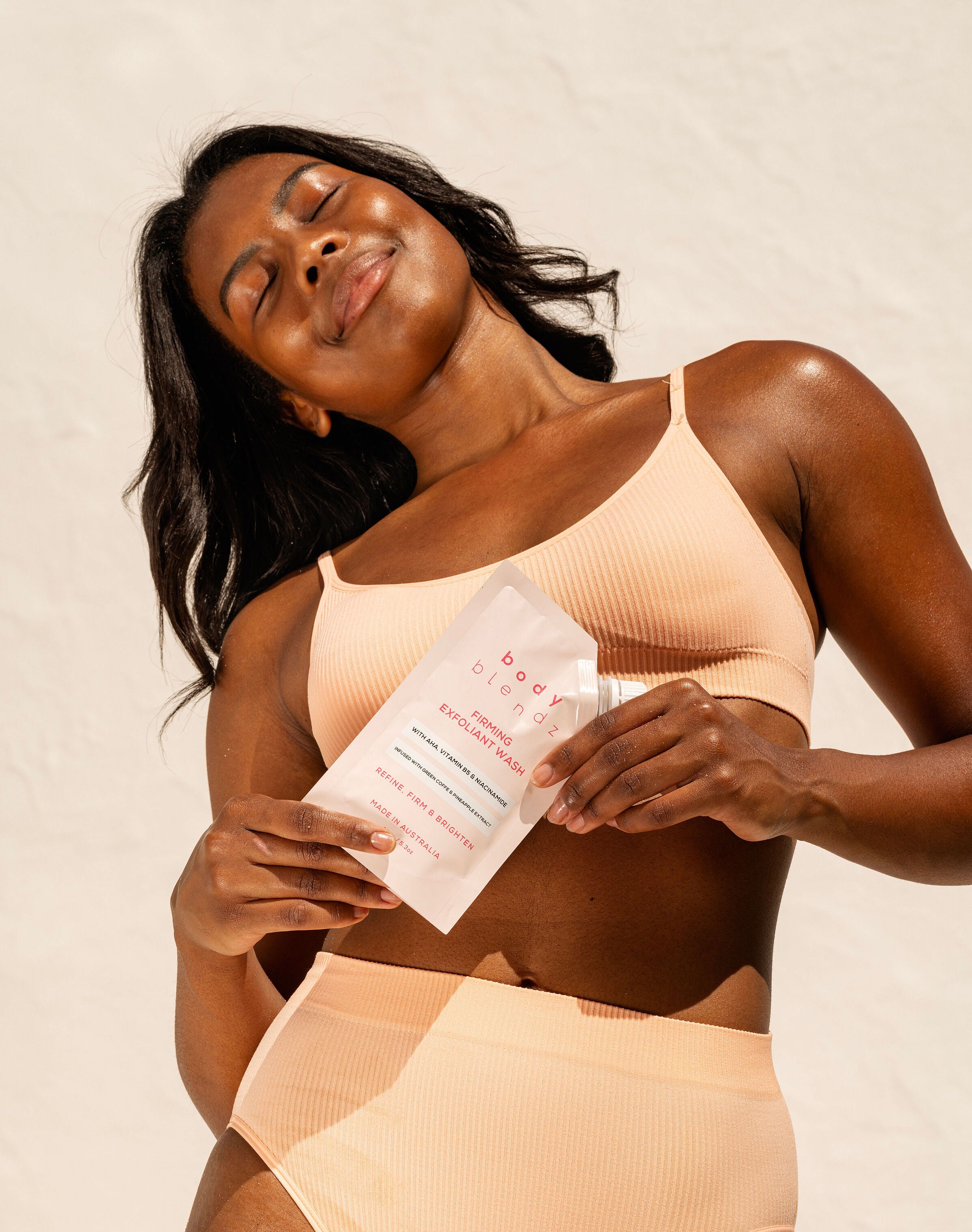 BodyBlendz firming exfoliant wash held by model, AHA body cleanser for smoother brighter and refined skin