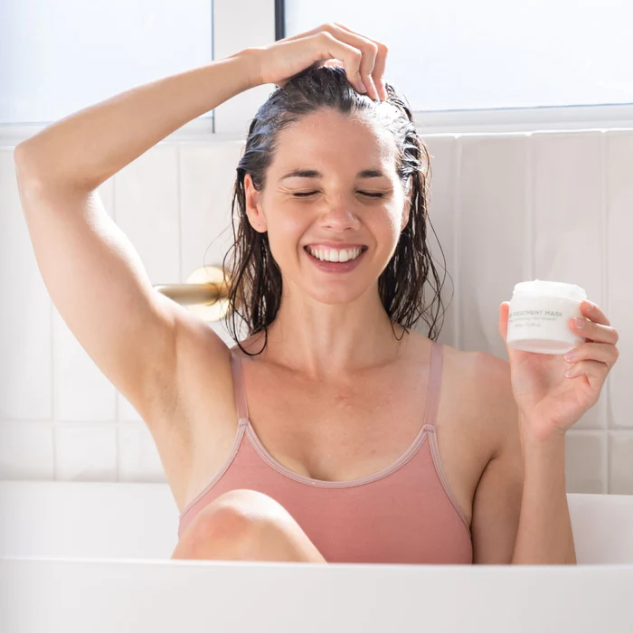 Woman applying BodyBlendz hair mask to wet hair in bath, hydrating treatment for smooth, healthy, shiny hair